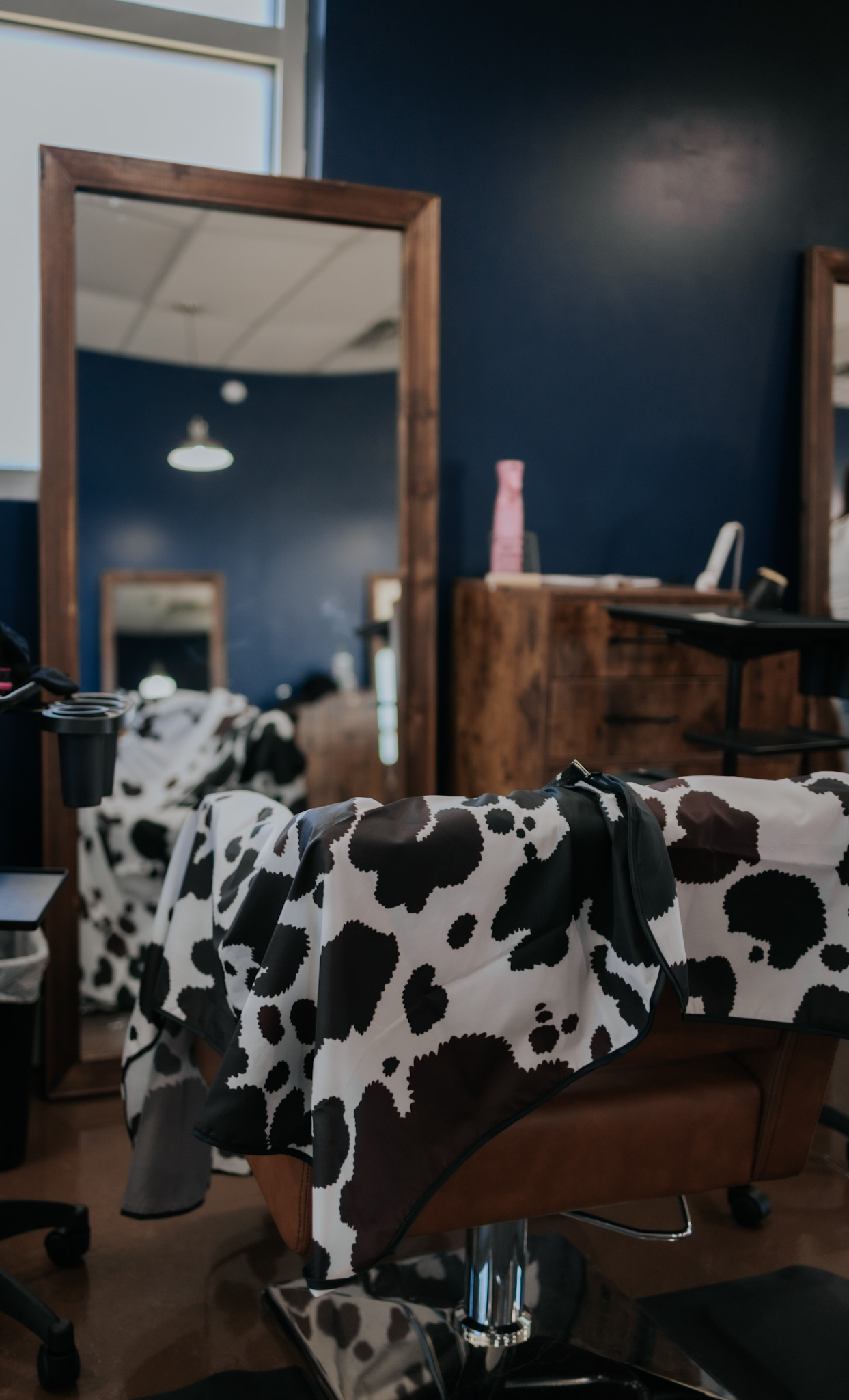 Cow-print salon chair and warm Western décor at Pearls & Whiskey in Goose Creek